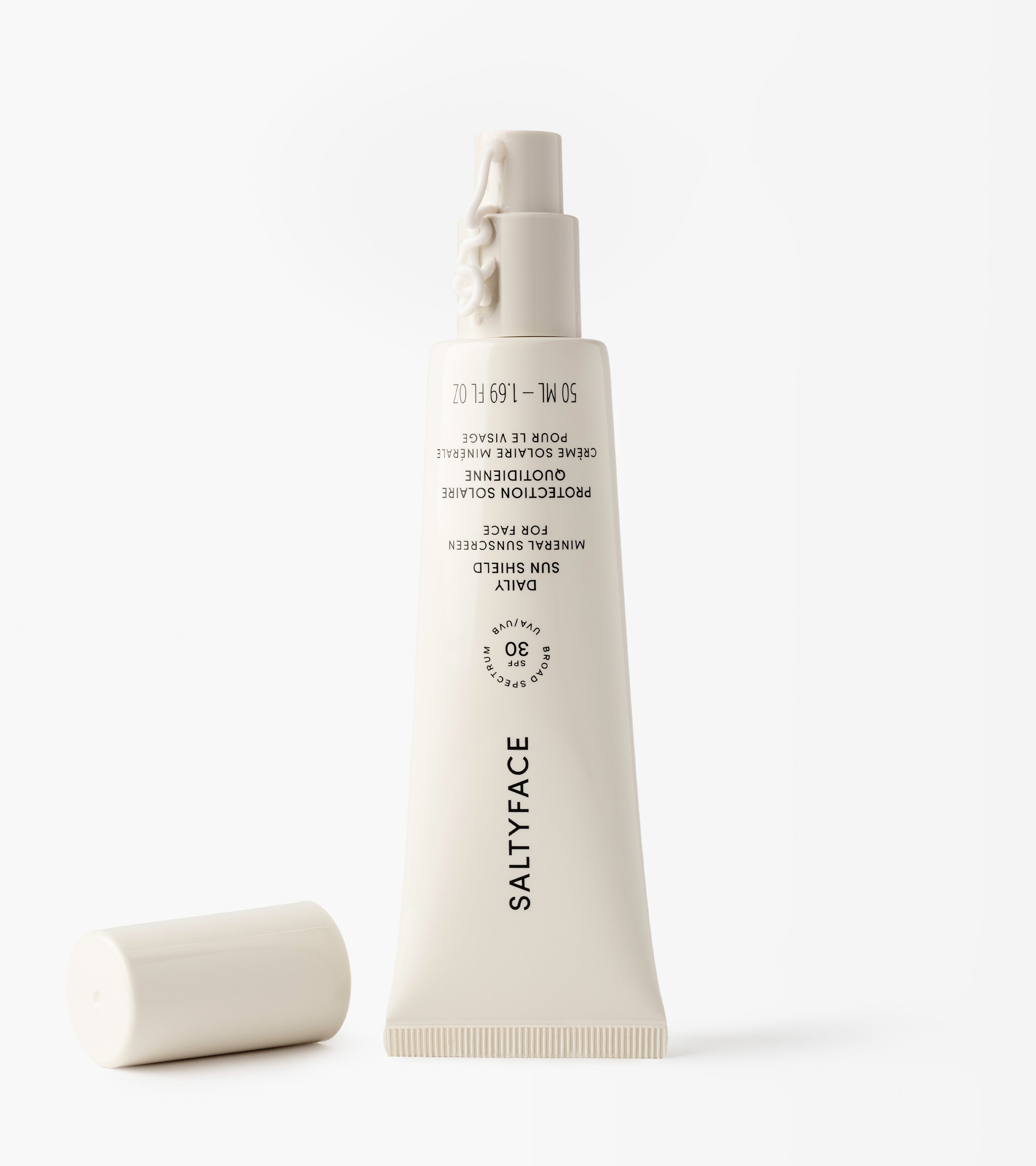 A white tube of Daily Sun Shield mineral SPF 30 sunscreen lies upside down on a white surface with its cap off and placed beside it.