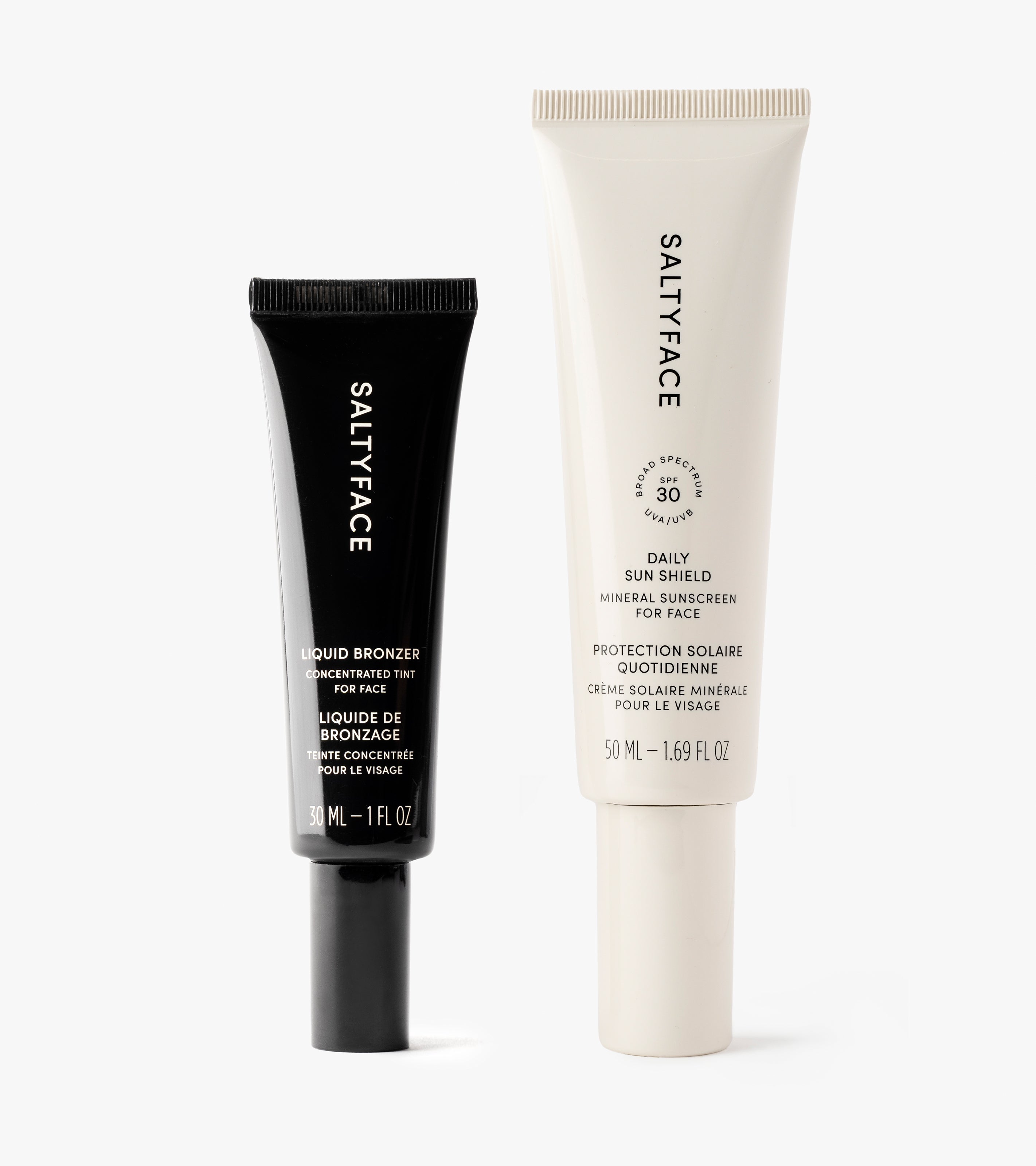 Two Sunscreen & Bronze tubes stand upright: a black Liquid Bronzer (30 ml) and a white Daily Sun Shield Mineral Sunscreen SPF 30 (50 ml), both providing sun protection, displayed on a white background.