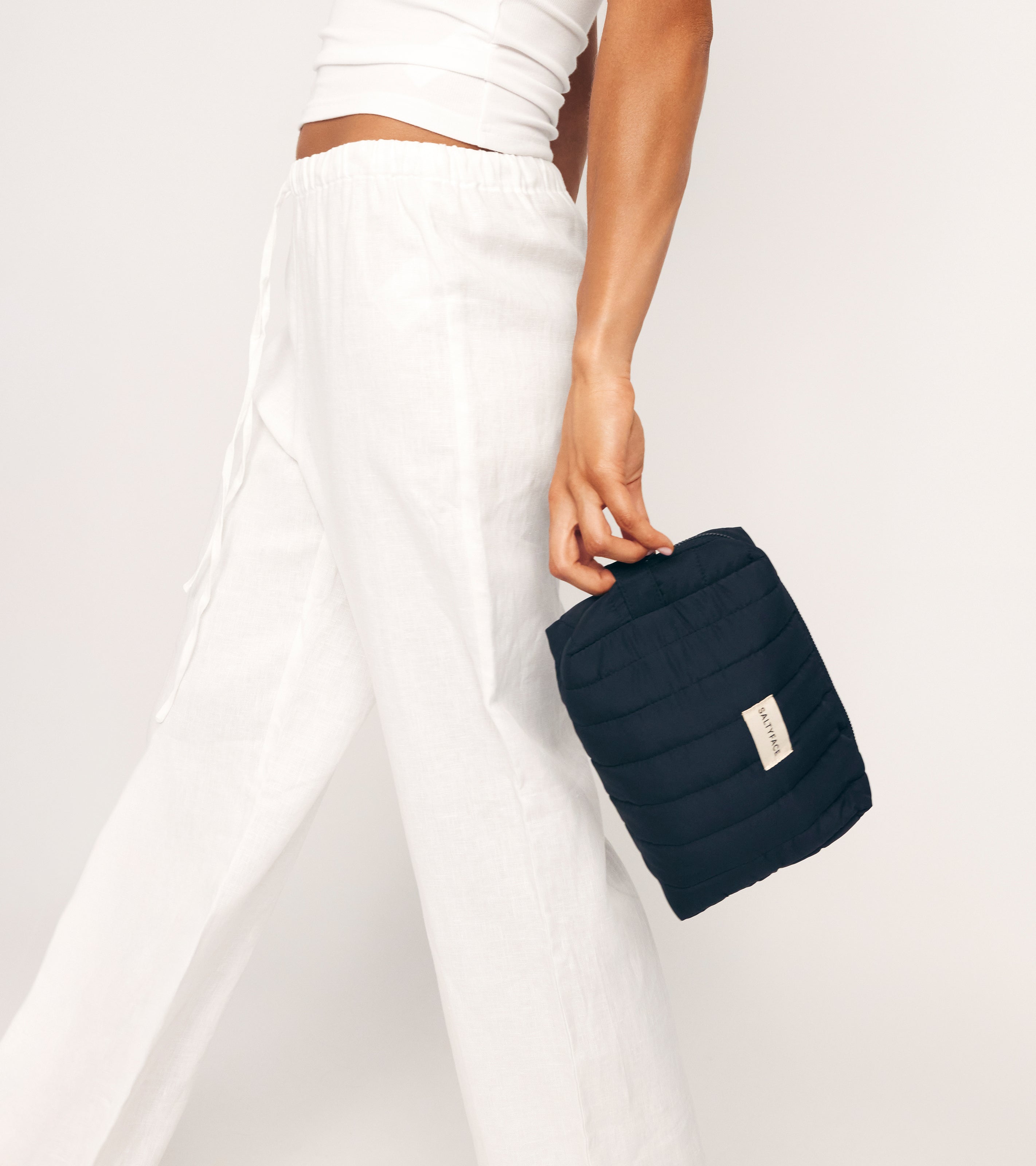 A person in white pants holds The Everywhere Bag, a spacious bag with a zip pouch—perfect for keeping essentials organized.