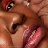 A close-up of a face displays glossy pink lips, smooth skin, and subtle red eye makeup. Text below says: “ROZ WEARS 19/99 – HIGH SHINE GLOSS ON LIPS.”.