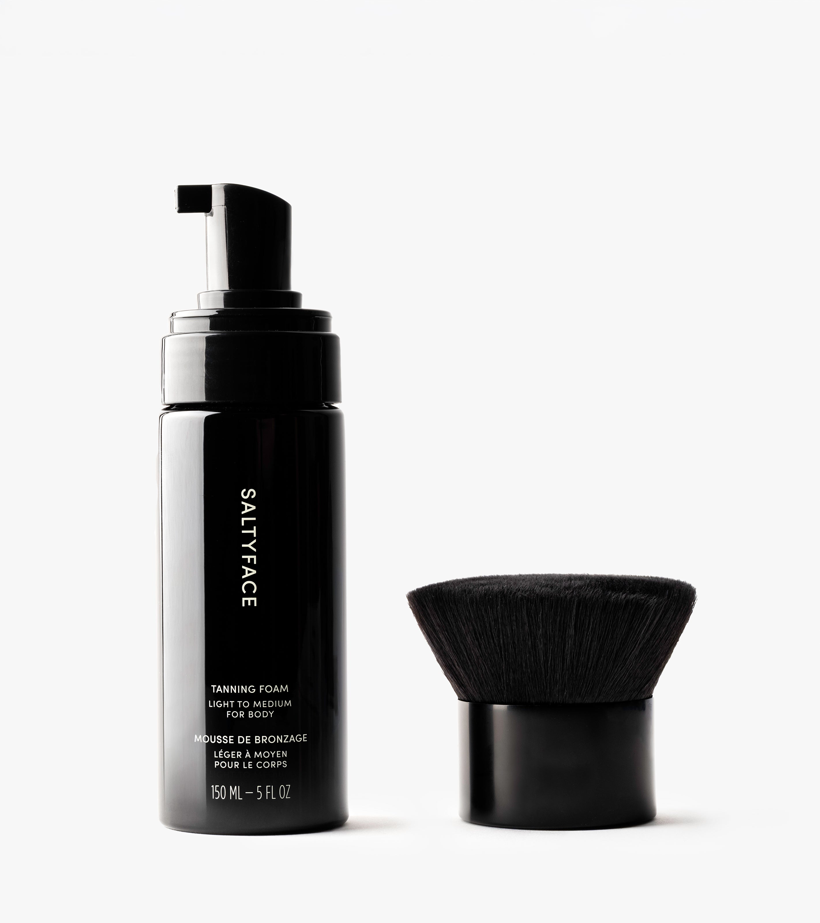 The Body Set, featuring a black bottle of Tanning Foam with a pump and a round body brush, sits on a white background—everything you need for a flawless, sun-kissed tan.