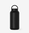 The Day Bottle is a matte black glass water bottle with a round cap and loop handle. SALTYFACE is embossed vertically on the side. Perfect for summer hydration, it features a plain white background.