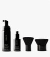 The Complete Face & Body Set features four black beauty essentials on a white background: a tanning foam bottle with pump, tanning water spray bottle, and two short-handled kabuki brushes for the ultimate tan.