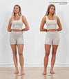 A young woman stands barefoot in front of a white wall, shown in side-by-side photos labeled Before and After. She wears a light gray tank top and shorts, displaying a natural-looking, full body tan from Tanning Foam in the After shot.