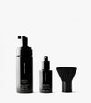 The Essential Face & Body Set by SALTYFACE includes three black skincare products—a Tanning Foam bottle with pump, a Tanning Water spray, and a dense-bristled face brush—displayed on a white background.