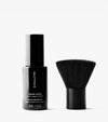 A black bottle labeled The Face Set sits beside a wide, black face brush on a white background, ready to help you achieve a flawless face tan.