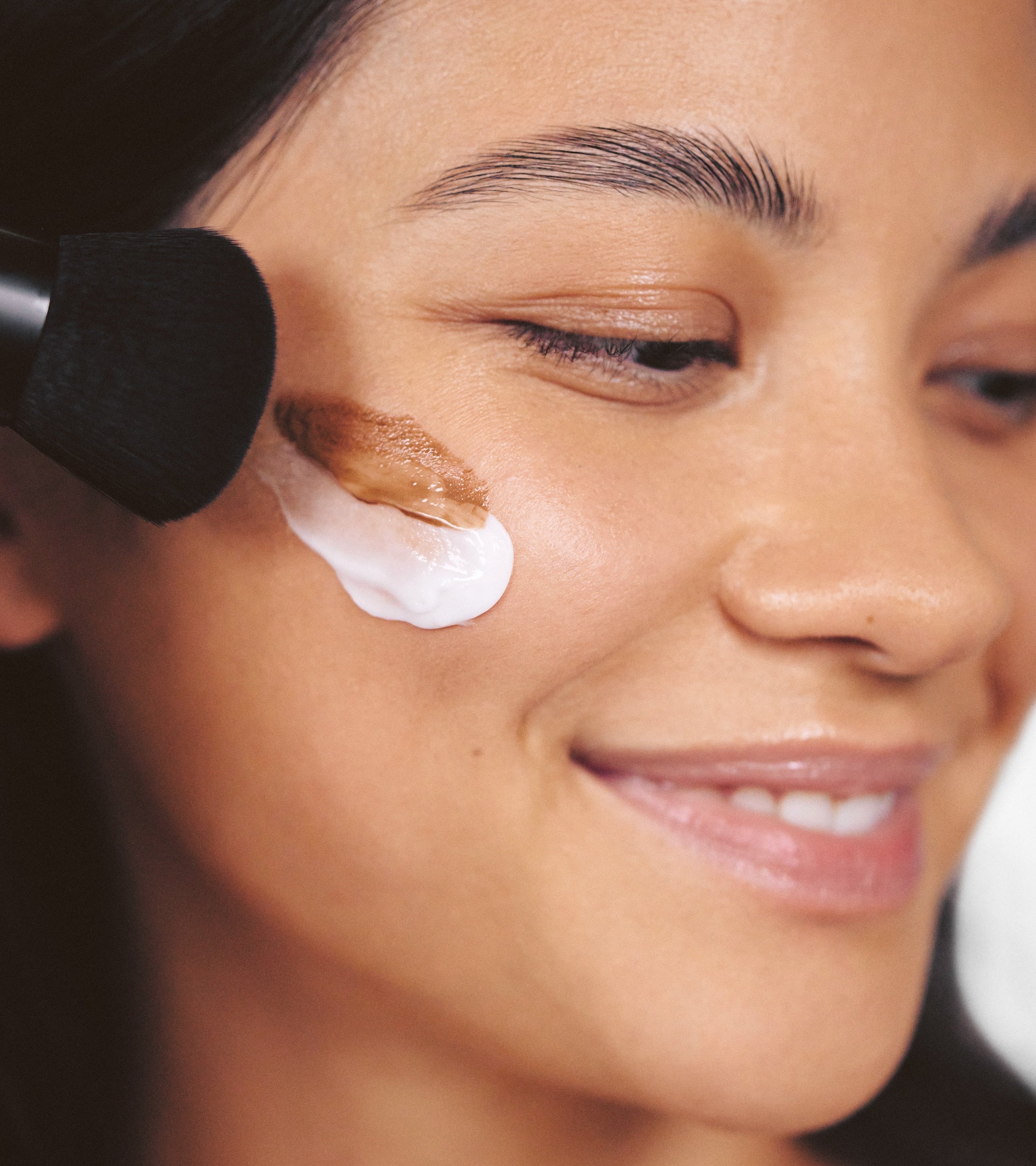 A model applies Daily Moisturizer and Liquid bronzer across her cheek, while holding Brush No. 3 up to her face.