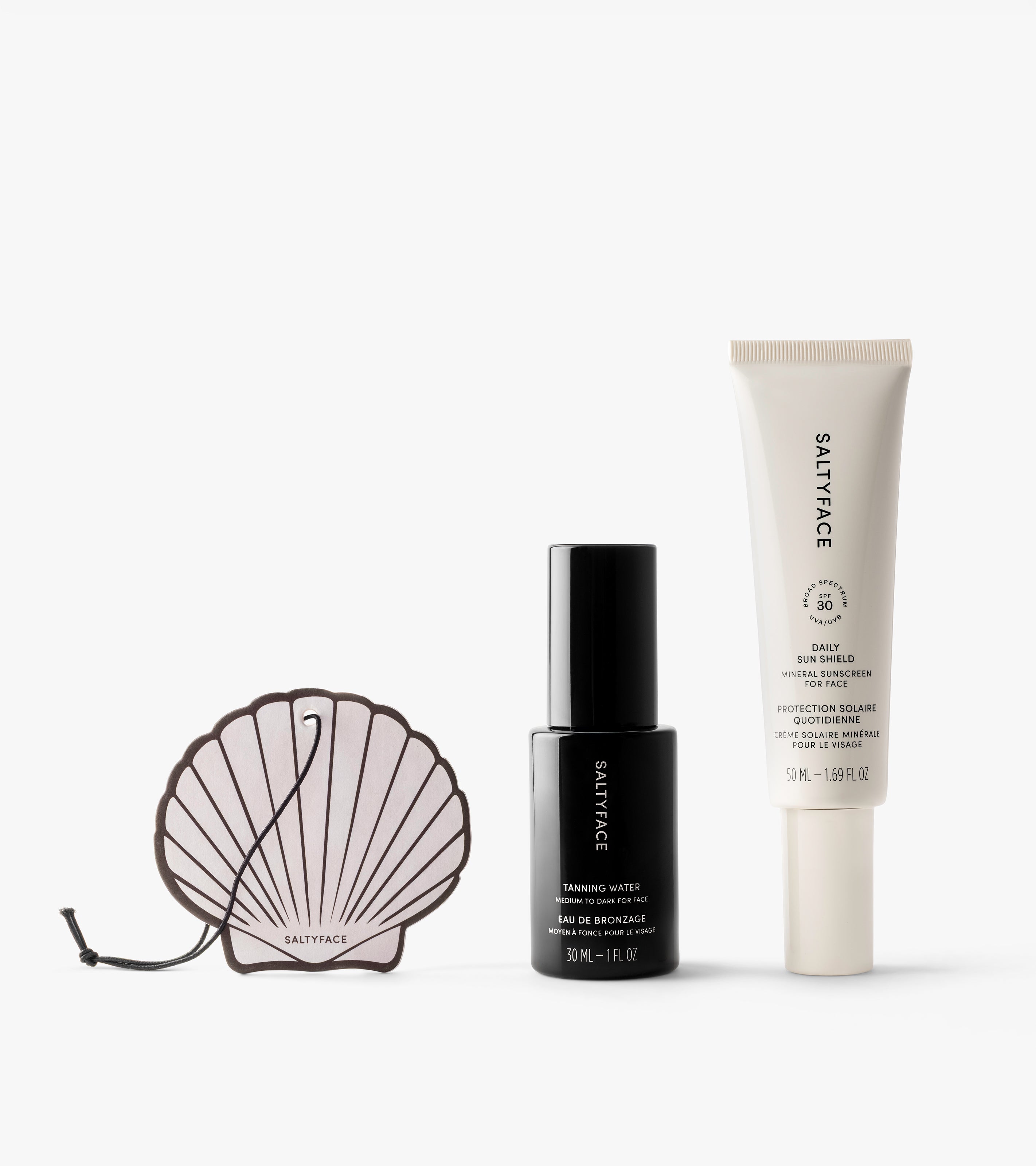 The Sun Set by Saltyface is displayed on a white background, featuring a shell-shaped dish, a black Tanning Water bottle, and a white Daily Skin Shield SPF 30 tube.