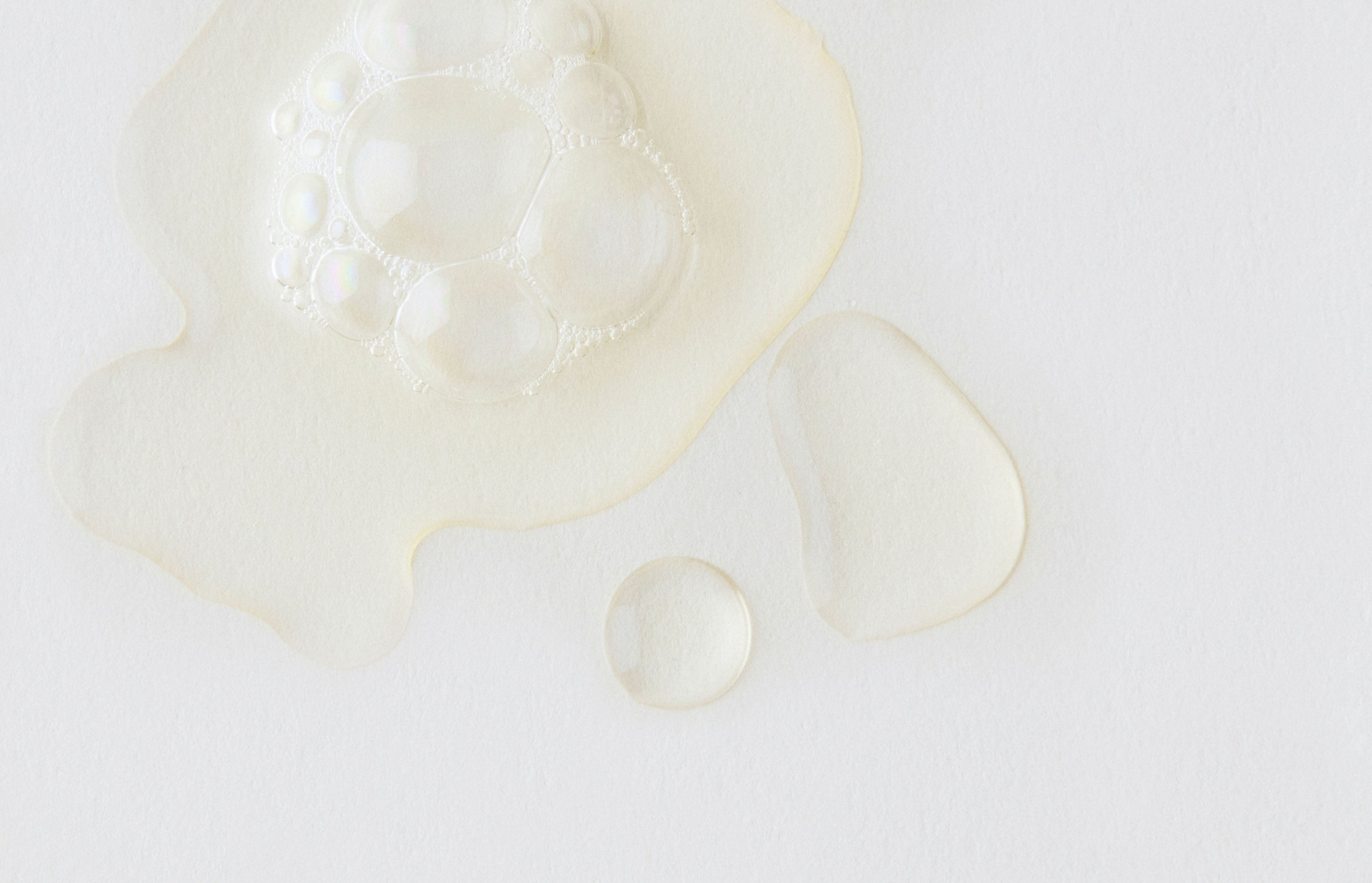 A thin, water-like liquid formula is shown in small pools against a white background. 