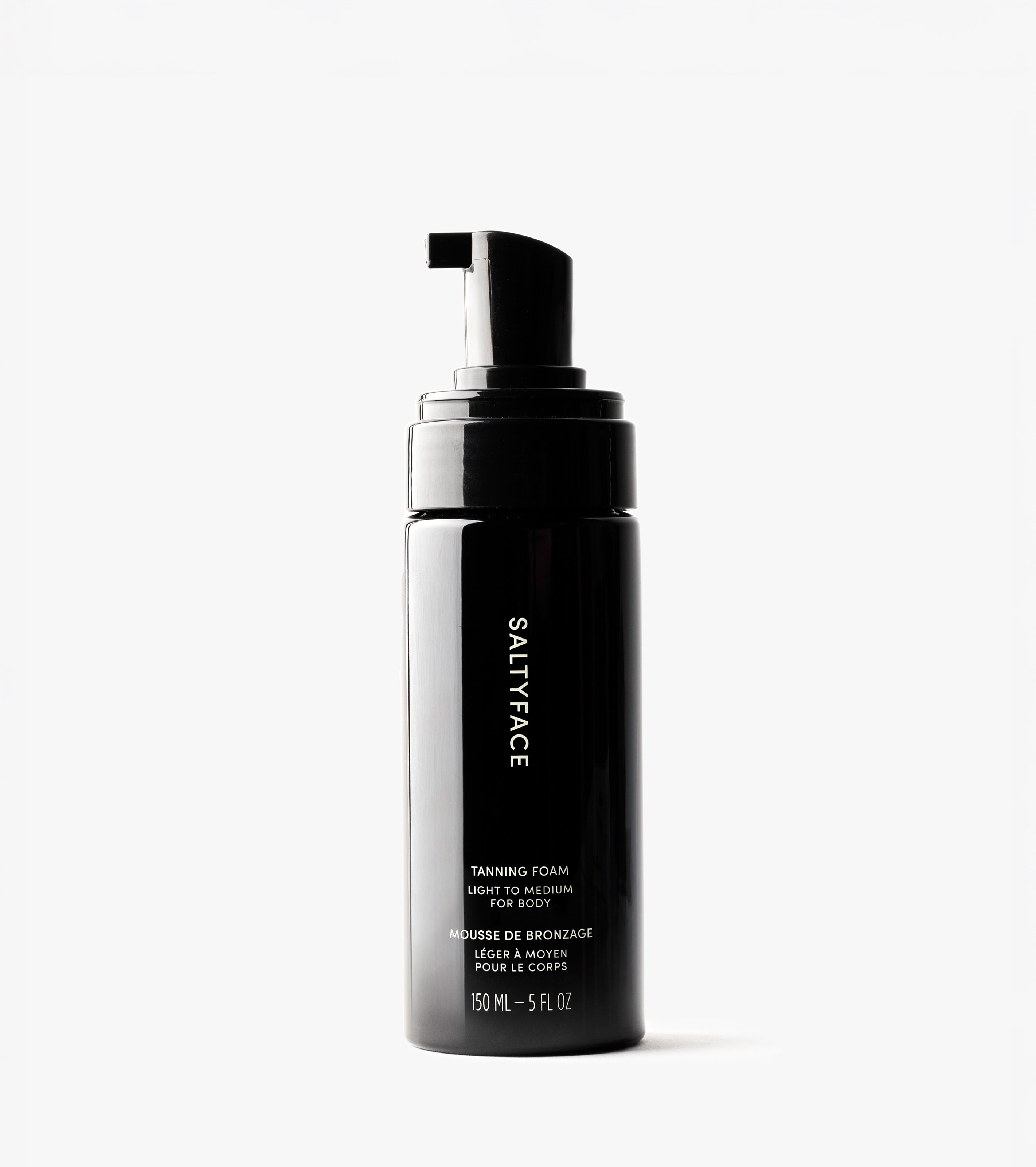 A black bottle of Tanning Foam with a pump dispenser is shown on a white background. The label notes its water-to-foam body care formula, delivering a light to medium tan in a 150 mL (5 fl. oz) size.