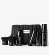 The Saltyface Set, featuring black skincare and makeup best-sellers for a natural sun-kissed look—brushes, bottles, tubes, and a foam dispenser—displayed before a black quilted bag with a white Saltyface label.