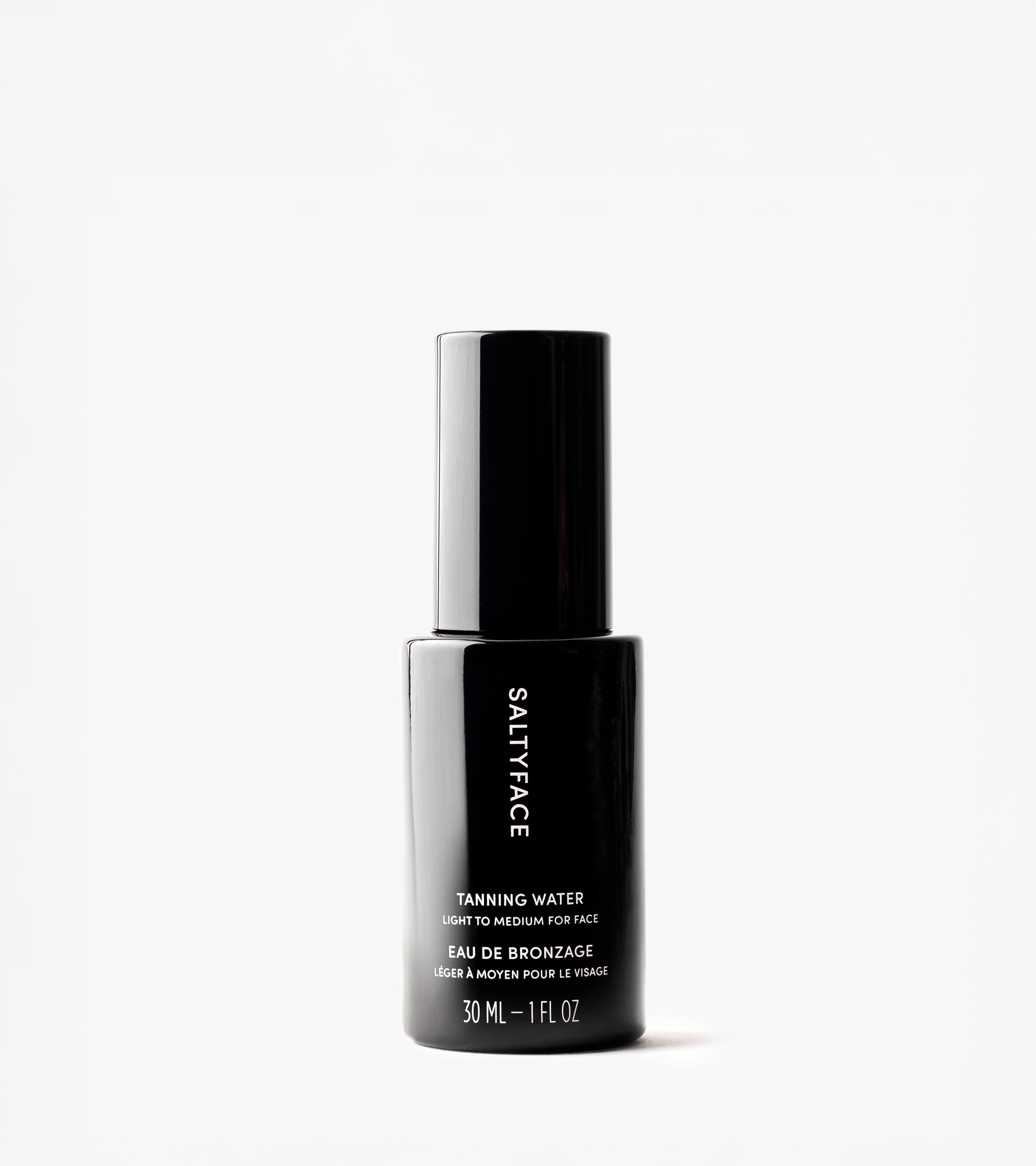 A black bottle of Tanning Water (30 ml/1 fl oz), labeled "Eau de Bronze," stands upright on a white background, offering a flawless, sun-kissed tan.