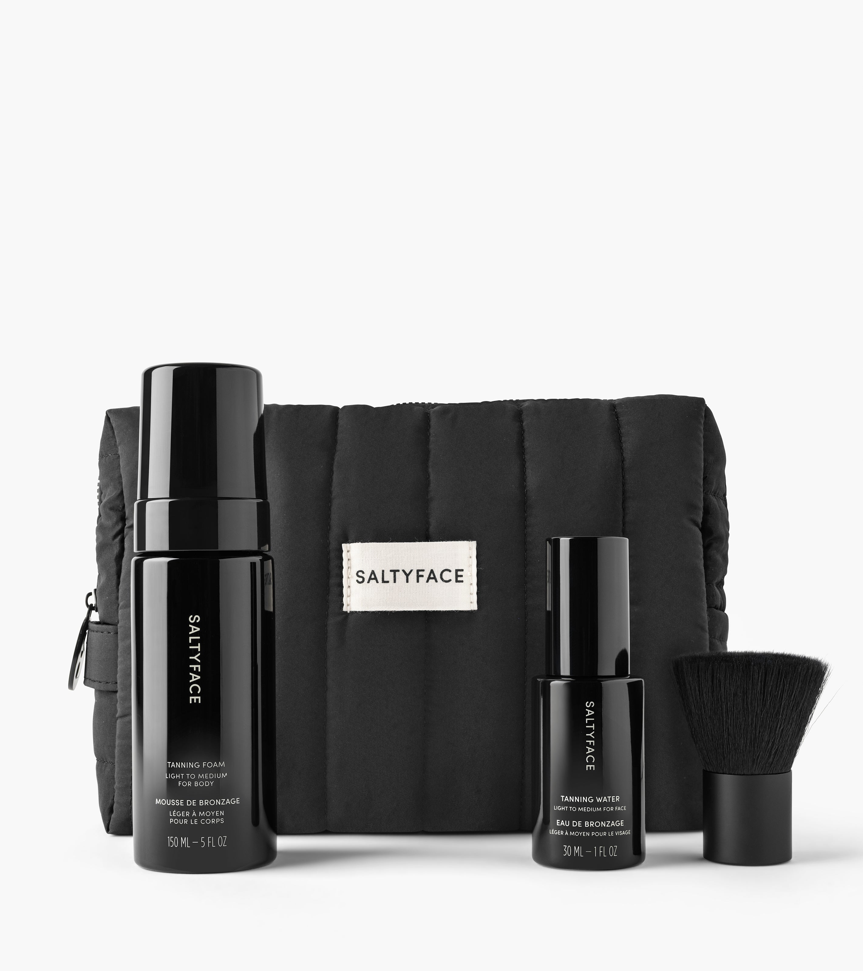 The Holiday Essential Set features black Saltyface skincare—including tanning foam, tanning water, a brush, and a padded pouch—arranged neatly against a white background.