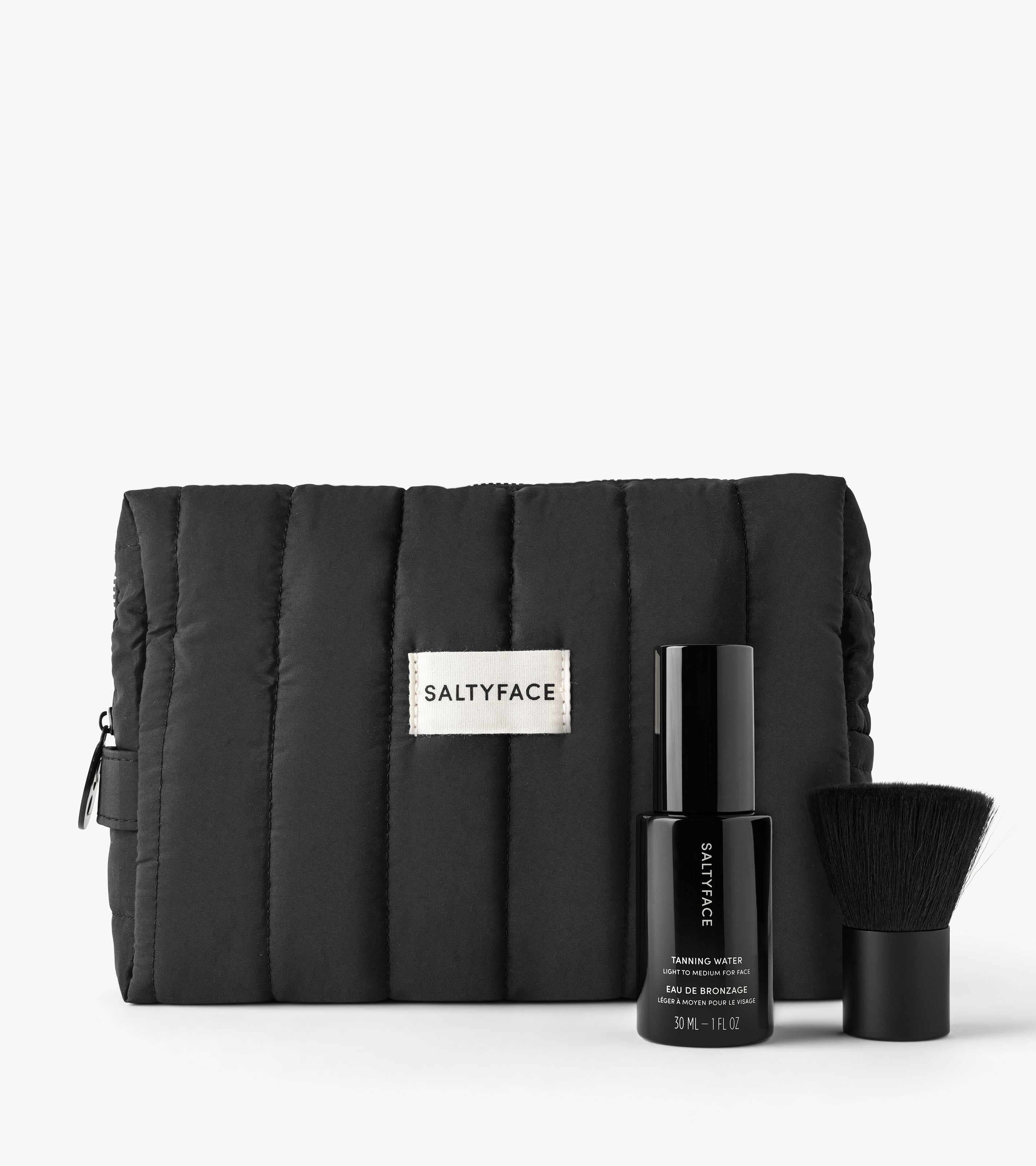 The Holiday Face Set includes a black quilted SALTYFACE cosmetic bag, a black bottle of SALTYFACE Tanning Water, and a small black makeup brush.