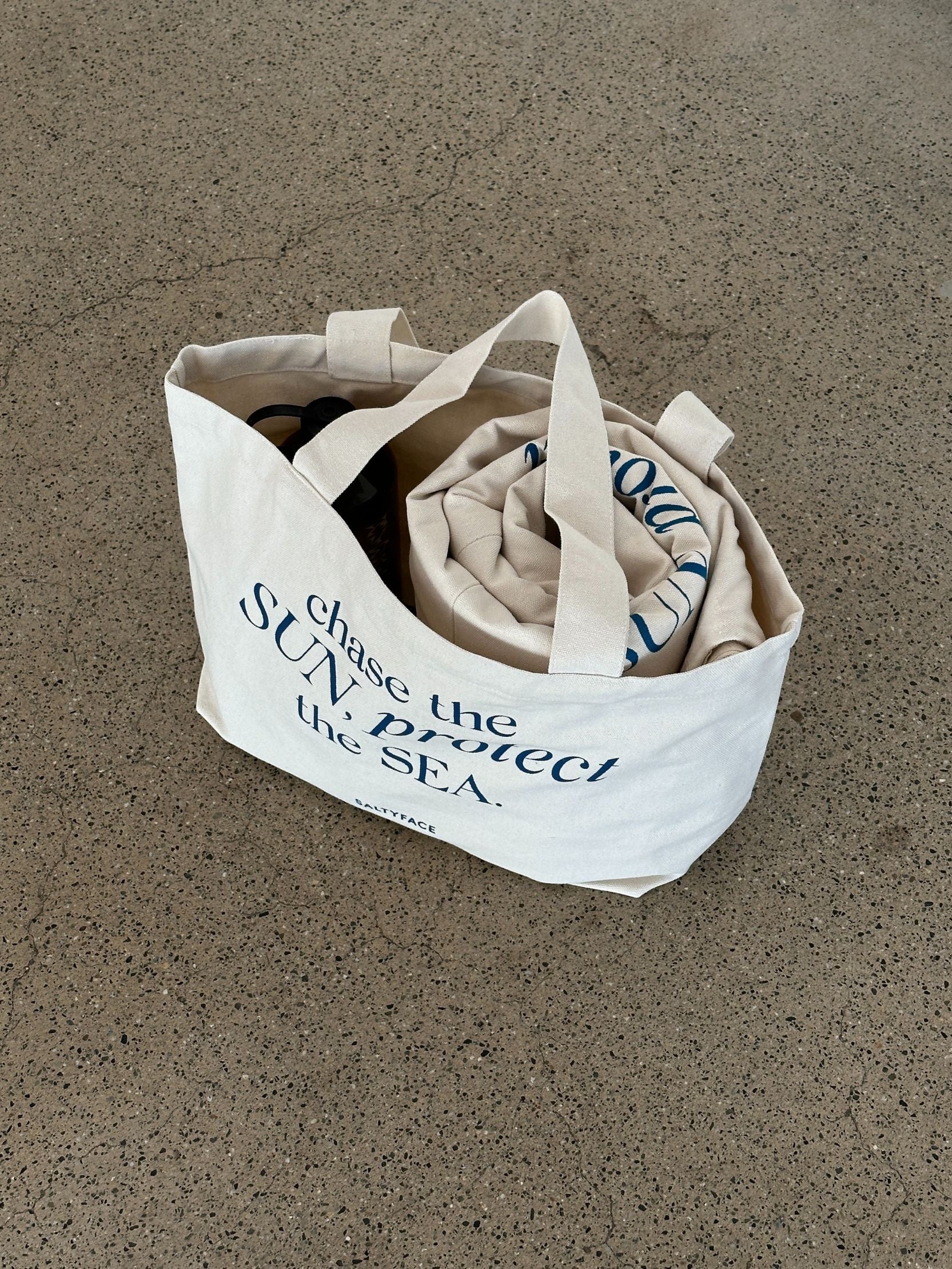 The Tote placed on the ground holding a water bottle and large blanket inside.