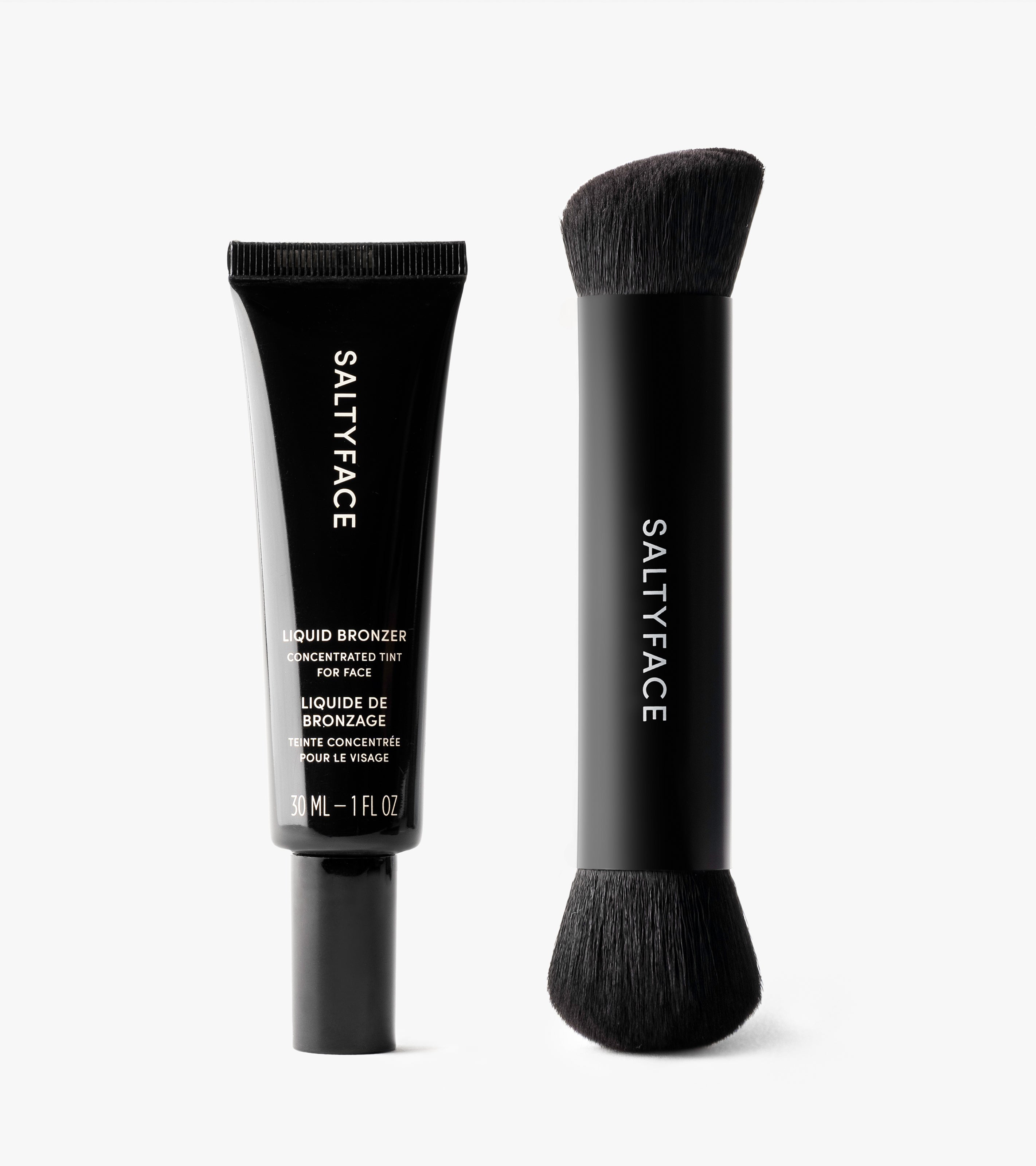 The Bronzing Duo includes a black tube of Saltyface Liquid Bronzer (30ml) and a double-ended bronzer brush with soft black bristles and a matching SALTYFACE handle, displayed upright on a white background.