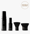 The Complete Face & Body Set, featuring Tanning Water, a Tanning Foam bottle, and two black makeup brushes, is displayed in a row on a white background. A circle at the top right says “Available in Coconut” for a flawless tan.