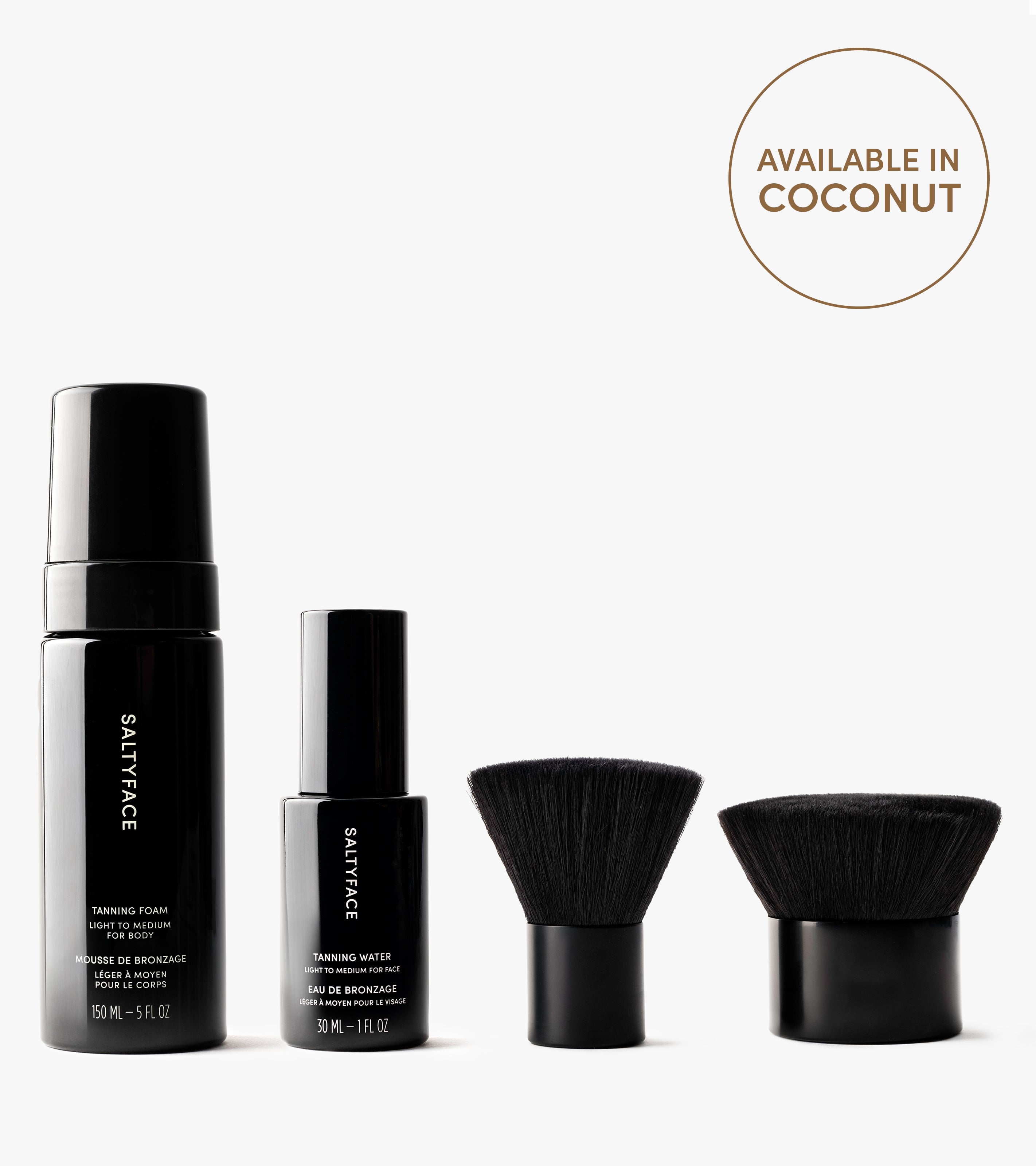 The Complete Face & Body Set, featuring Tanning Water, a Tanning Foam bottle, and two black makeup brushes, is displayed in a row on a white background. A circle at the top right says “Available in Coconut” for a flawless tan.