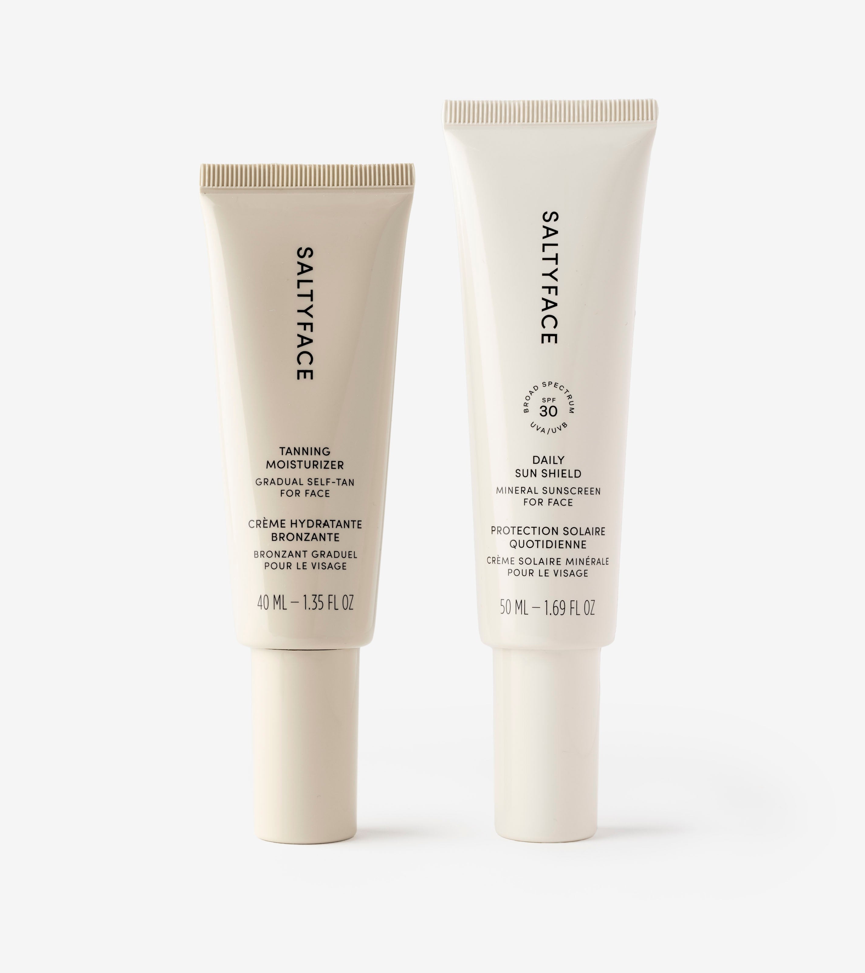 Two upright tubes of Sunscreen & Tan products: on the left, a 40 mL face tanning moisturizer; on the right, a 50 mL mineral Daily Sun Shield SPF 30 sunscreen. Both feature white tubes and sleek black text.