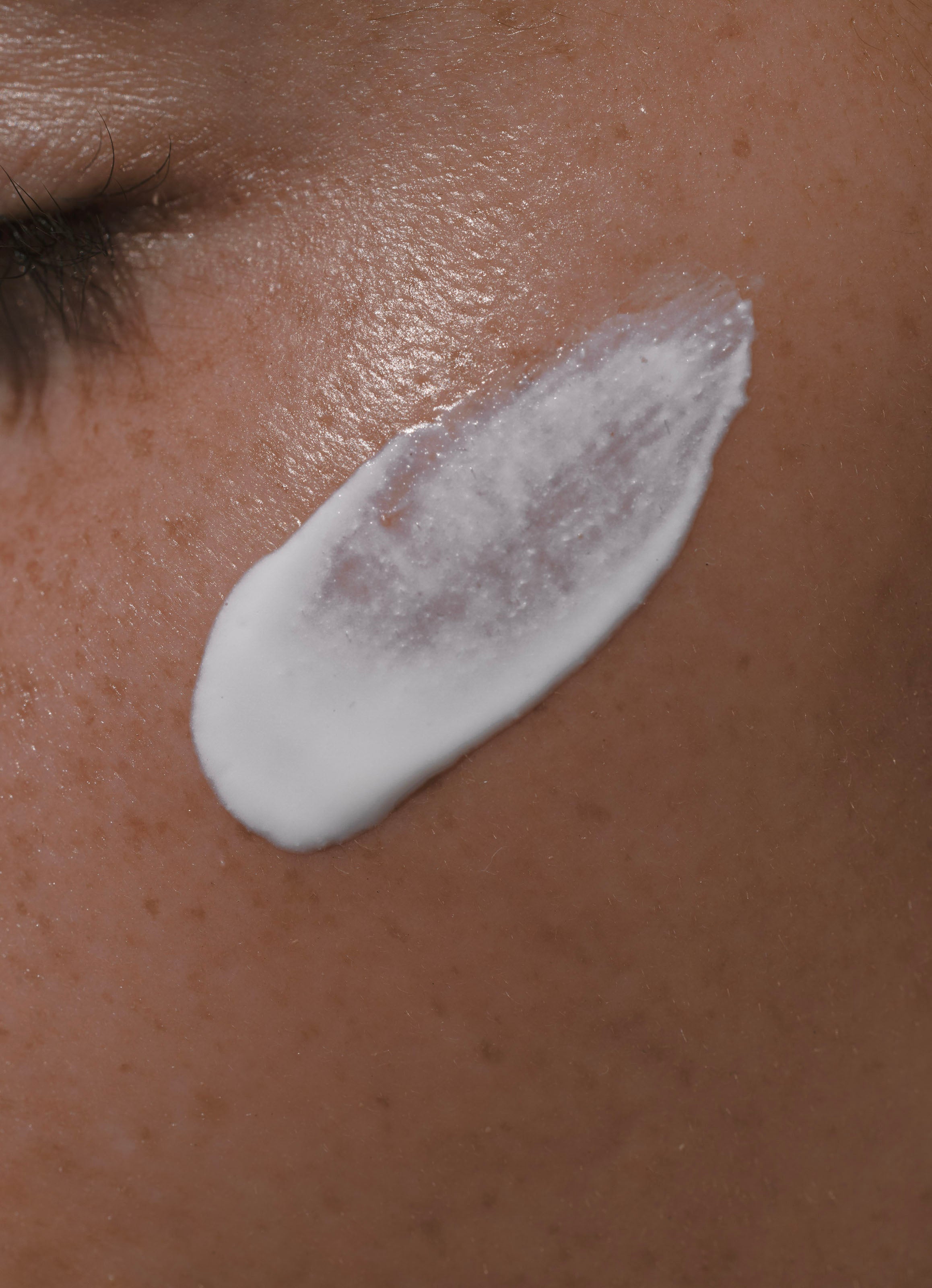 A close-up of a person’s freckled, brown cheek with Daily Sun Shield mineral sunscreen smoothly applied near the eye, providing gentle SPF 30 protection.